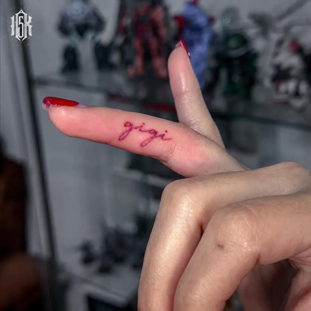 ตัวอักษร "gigi" หมึกสีแดง ลายมือเขียนบนนิ้ว บริเวณนิ้วชี้ โดยช่างหมิว — ผลงานจริงจาก 15K Tattoo ร้านสักบางแสน